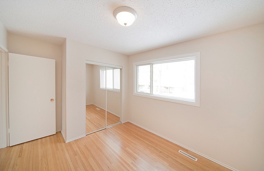 A room with a white ceiling, a door, a window, and a wooden floor.