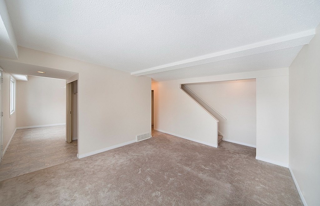 A room with a carpeted floor and a stairway leading to another room.