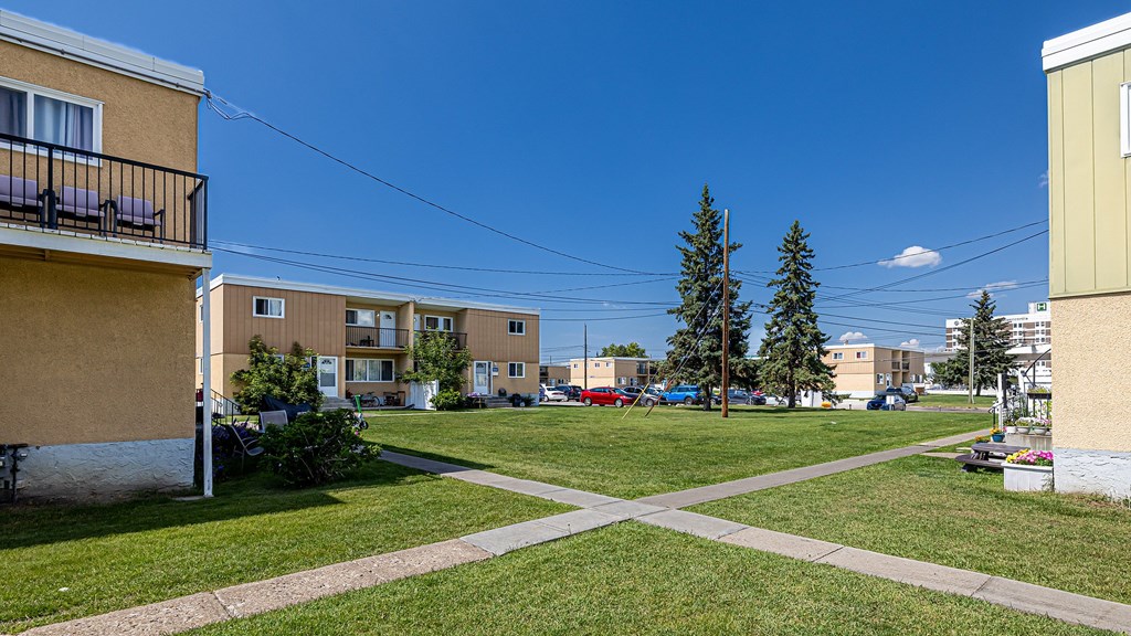 A sunny day at a small grassy park with apartment buildings in the background.