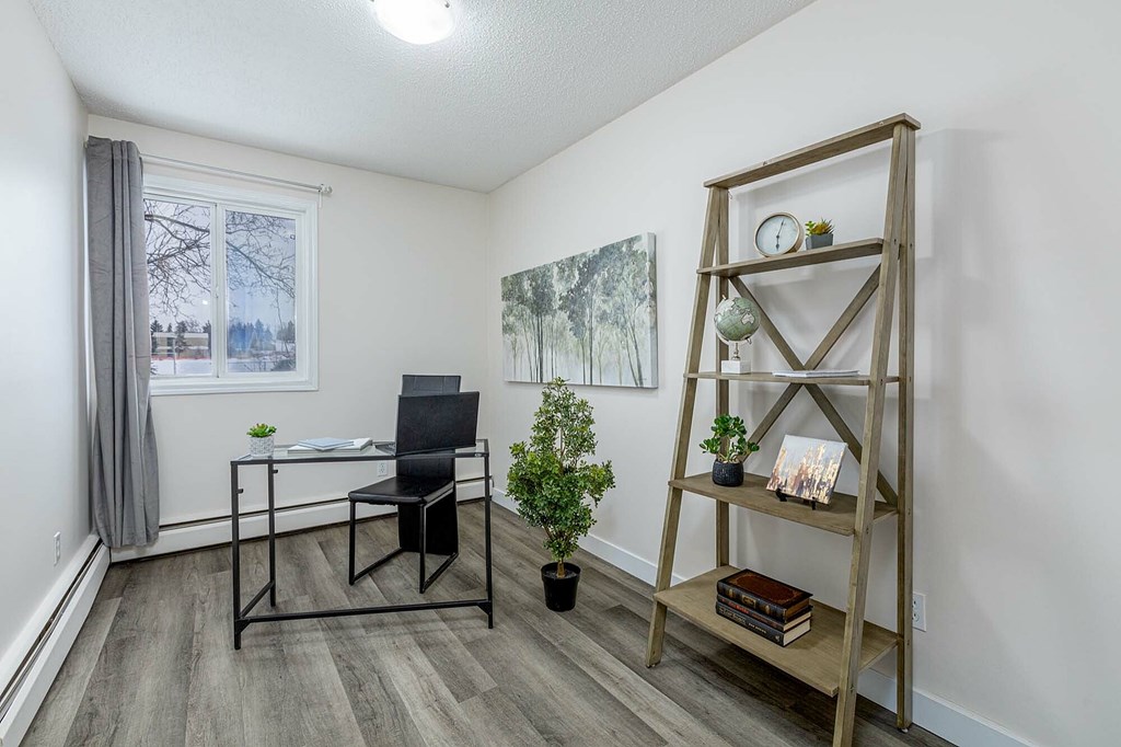 A room with a chair, a table, a plant, and a shelf with books and a candle.