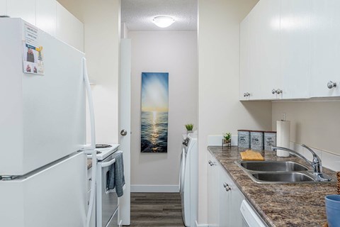 A kitchen with a white fridge and a painting of a sunset on the wall.