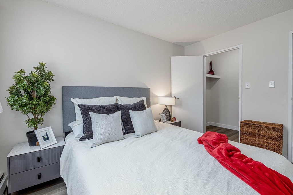 A bedroom with a bed, nightstand, and a plant.