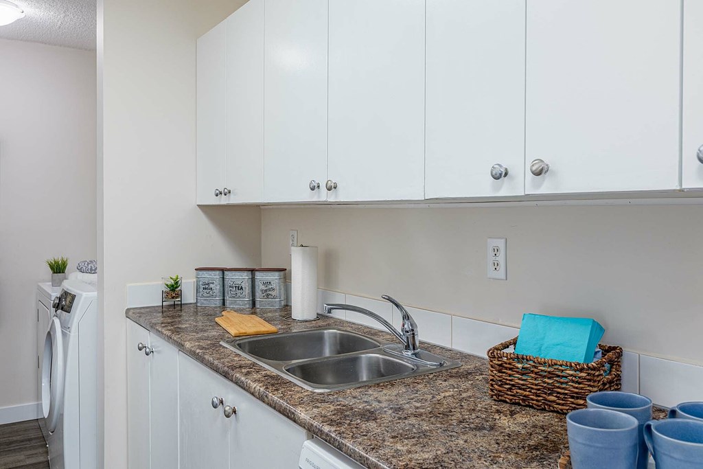 A kitchen with a washing machine and a basket of blue cups.