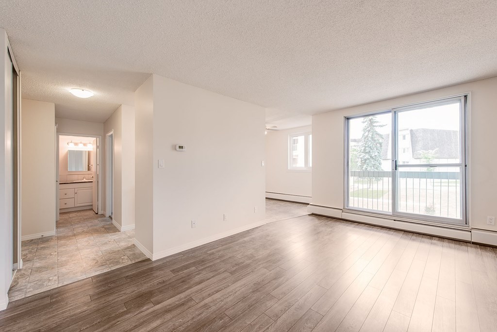 A large empty room with wooden floors and a view of a balcony through the window.