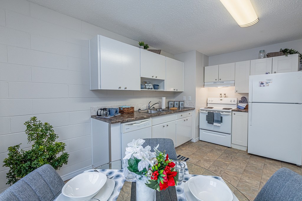 A kitchen with white cabinets and appliances, a dining table set with plates and a vase of flowers.