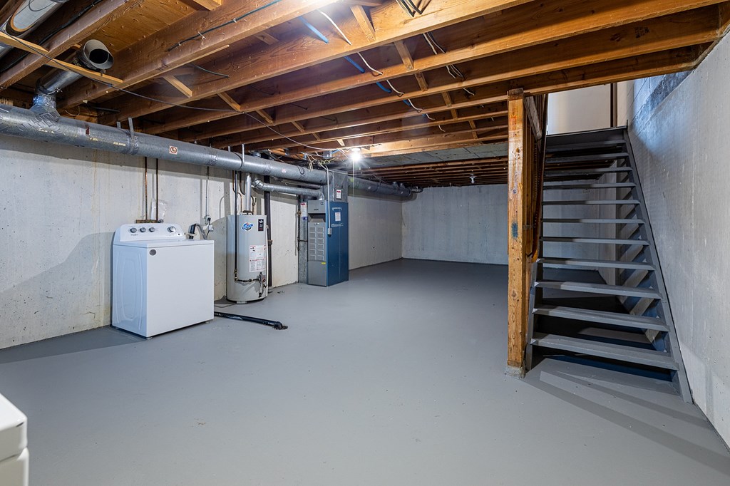 A spacious basement with a staircase, a white refrigerator, and a blue cabinet.