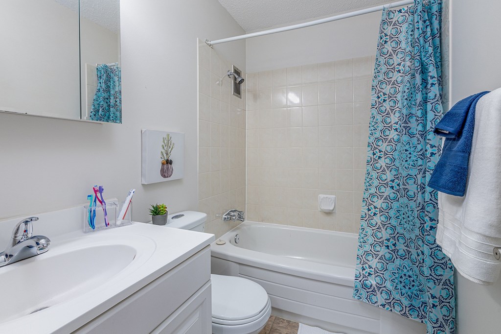 A bathroom with a white sink, toilet, and bathtub with a blue shower curtain.