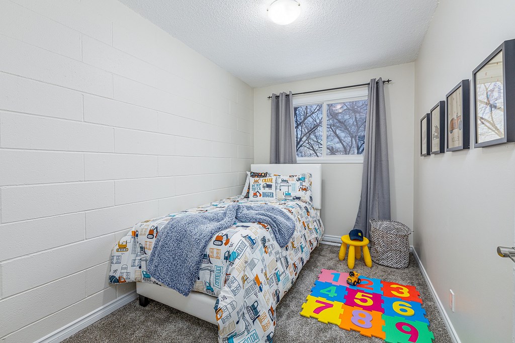 A small bedroom with a bed, a carpet, a window, and a wall hanging.