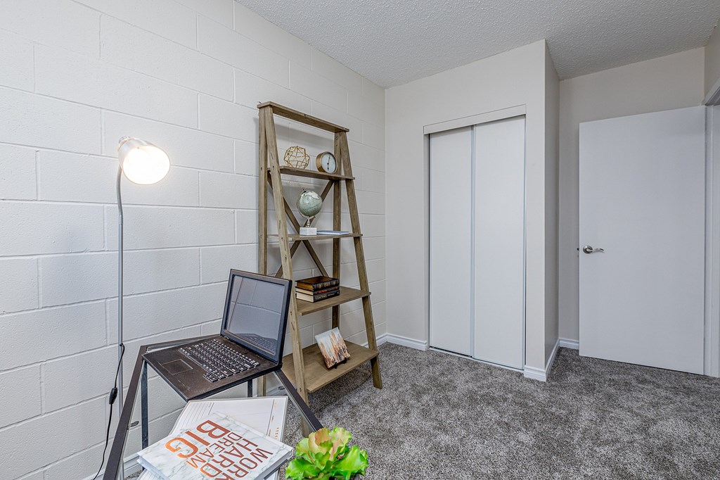 A room with a laptop on a table and a shelf with books and decorations.