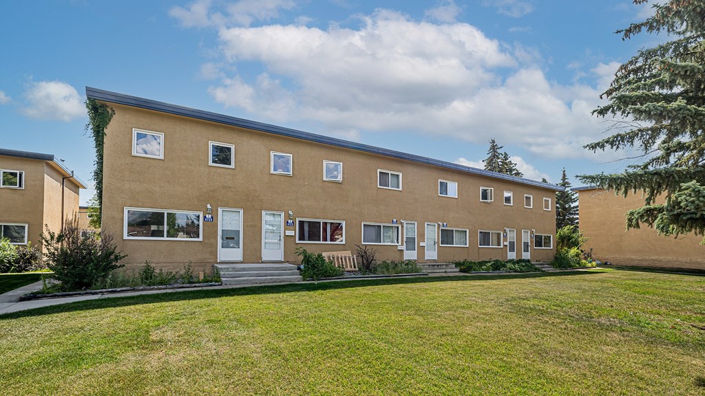 A building with a white door and windows is surrounded by a green lawn.