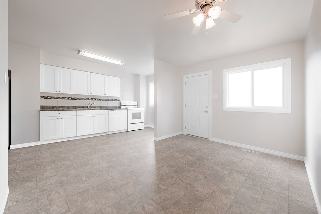 A spacious empty room with a ceiling fan and a window.