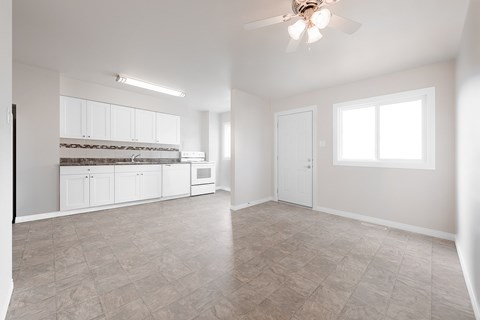 A spacious empty room with a ceiling fan and a window.