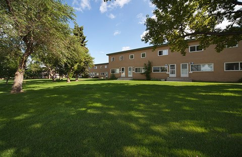 A grassy area in front of a building with trees.