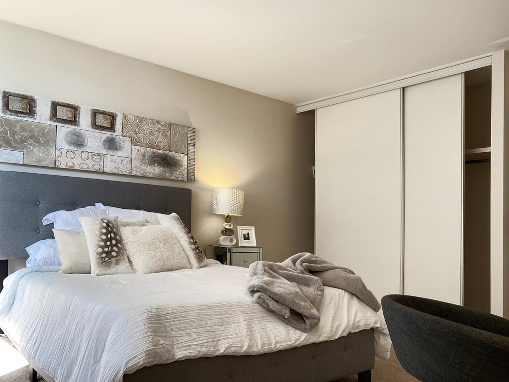 A bedroom with a bed, a lamp, a wall art, and a chair.