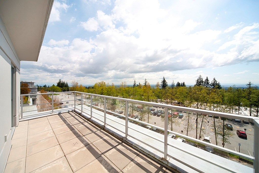 A balcony with a view of a parking lot and trees.