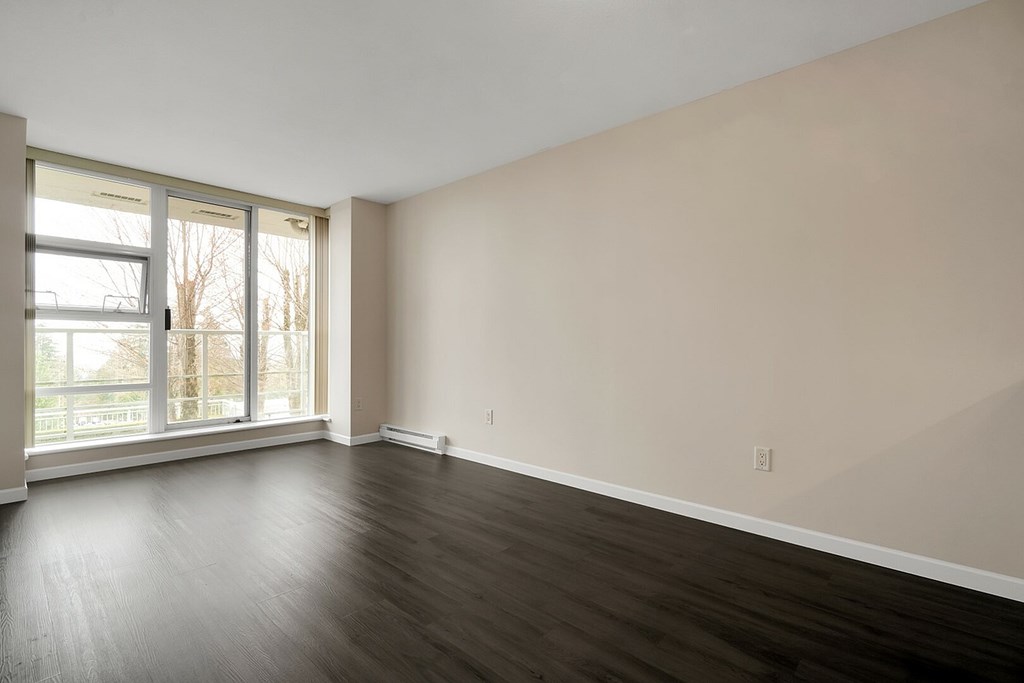 Empty room with wood flooring and large windows.