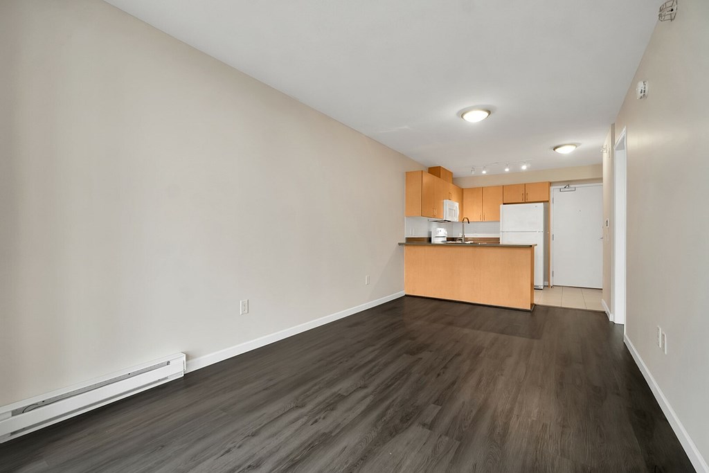 A room with a wooden floor and a kitchenette in the background.
