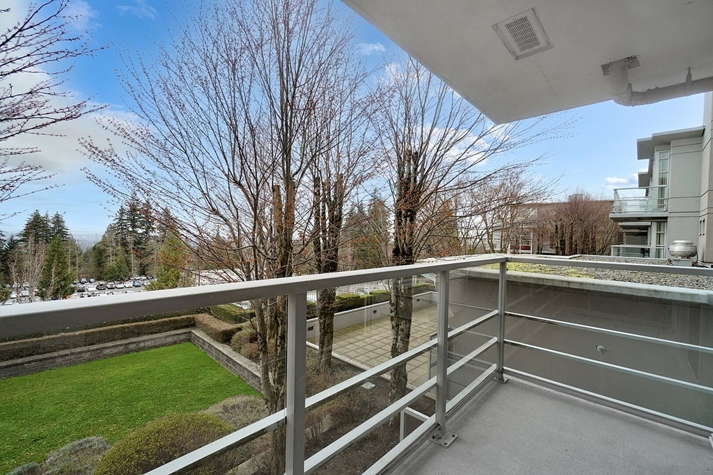 A balcony with a metal railing overlooks a green lawn and trees.