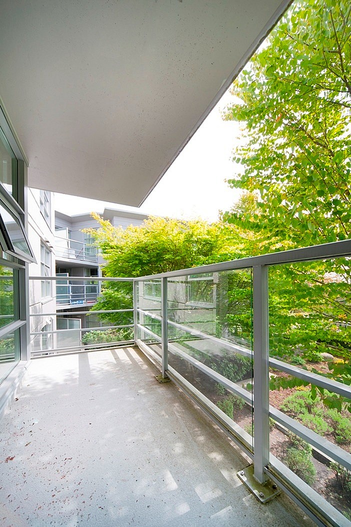 A balcony with a metal railing and glass panels overlooking a green tree.