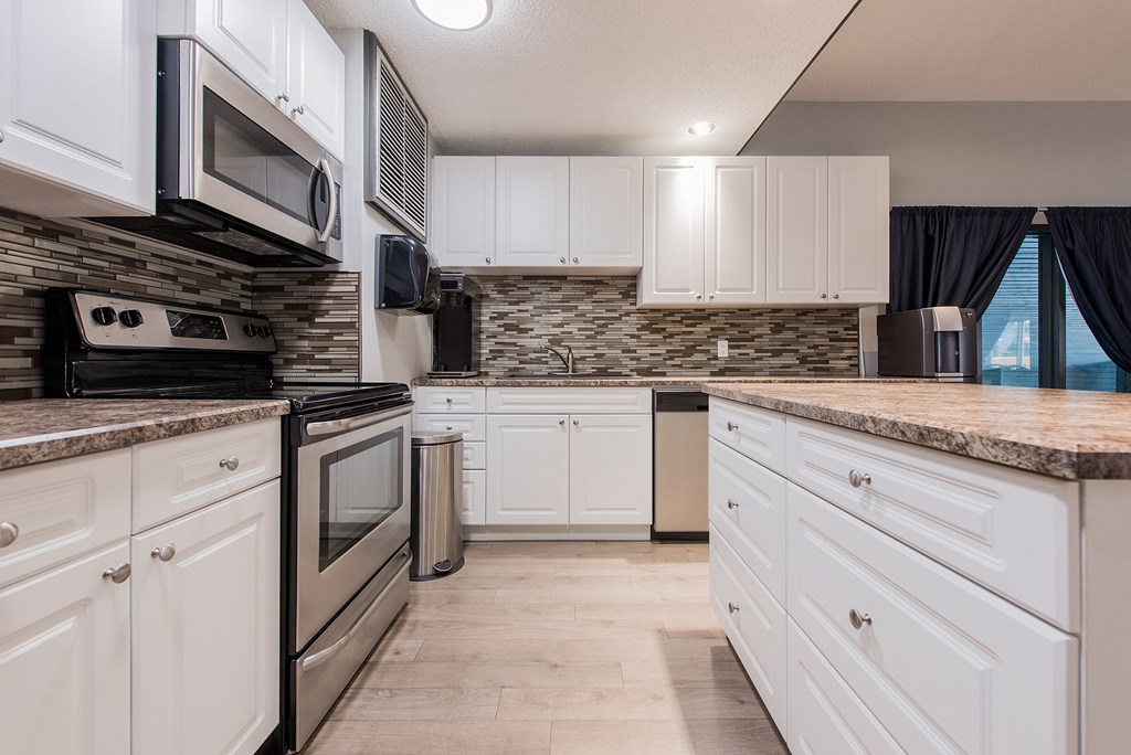 A kitchen with white cabinets and a stone backsplash.
