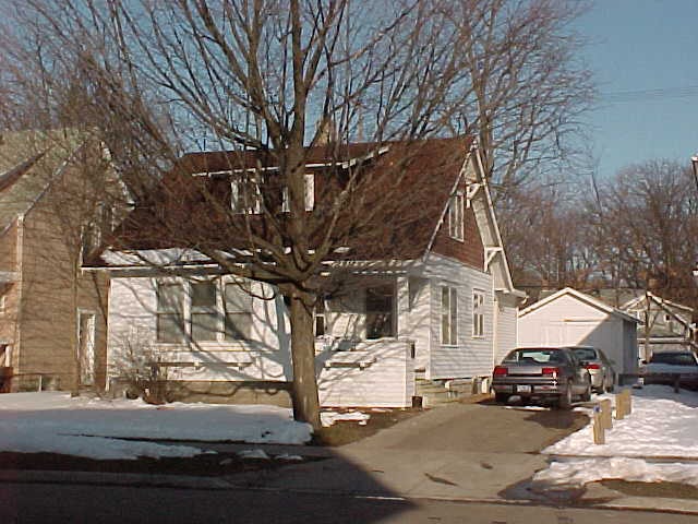 A white house with a brown roof and a tree in front.