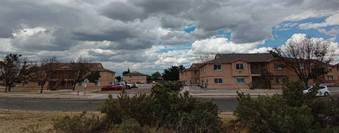 A cloudy day at a residential complex with apartment buildings and cars parked outside.