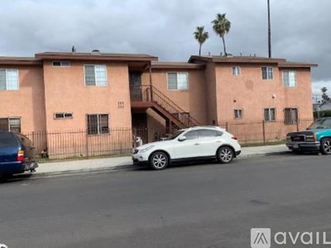 A white car is parked in front of a pink building.