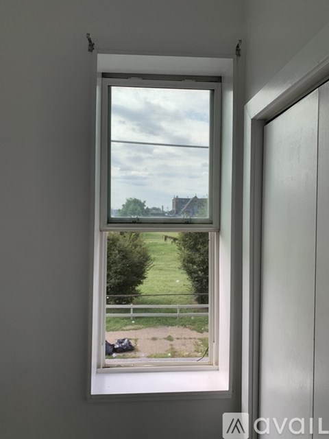 A window with a view of a green lawn and a building in the distance.
