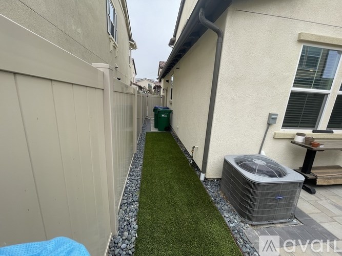 A narrow alley with a green trash bin and a grey air conditioning unit.