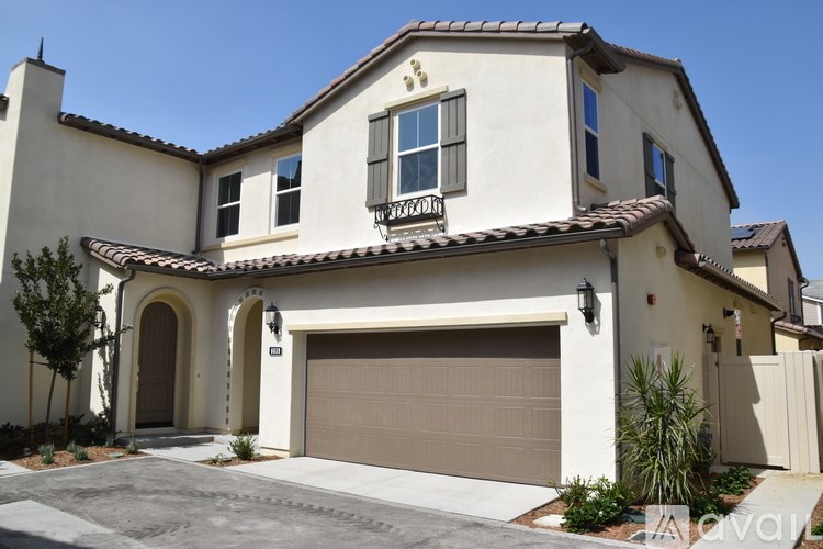 A two-story house with a garage door and a balcony on the second floor.