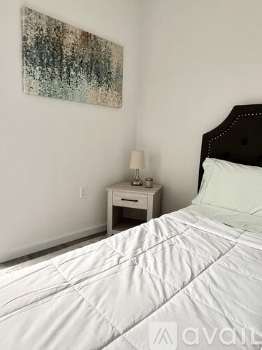 A bedroom with a white bed and a painting on the wall.