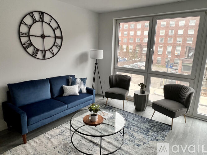 A living room with a blue sofa, two chairs, a coffee table, and a large clock on the wall.