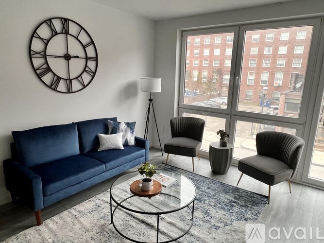 A living room with a blue sofa, two chairs, a coffee table, and a large clock on the wall.