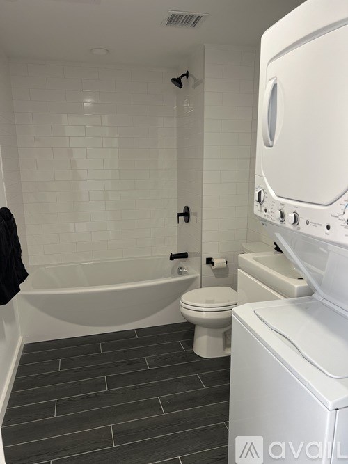 A white washing machine is in a bathroom with a toilet and tub.