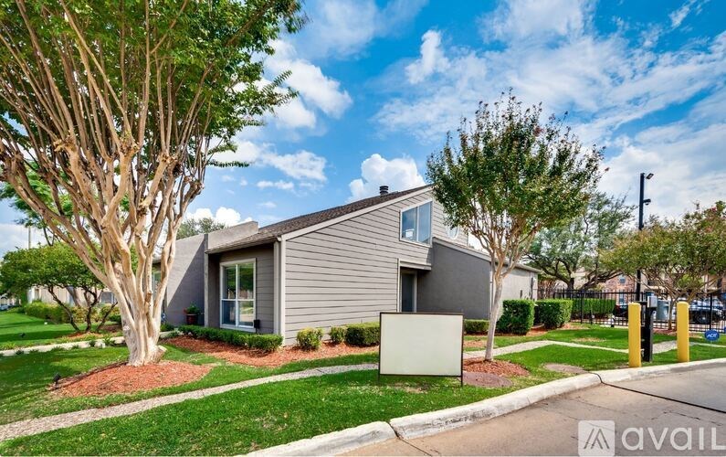 A house with a grey exterior is surrounded by greenery and a clear blue sky.