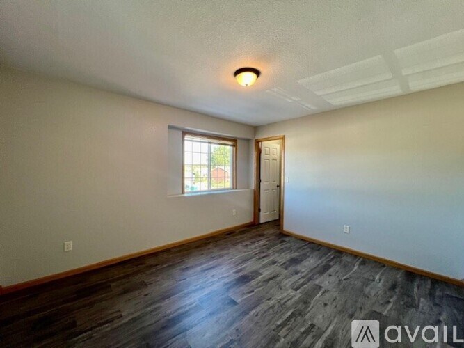A room with wooden flooring and a window with a view of trees.