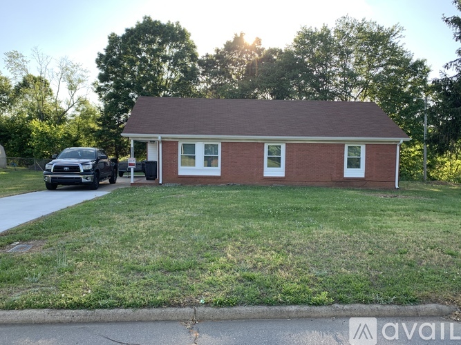 A small red brick house with a white door and windows is in front of a parked car.