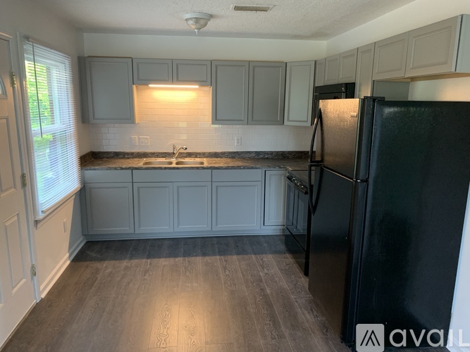 A kitchen with a black refrigerator and wooden floors.