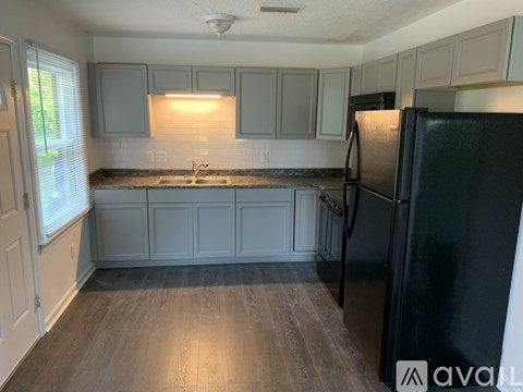 A kitchen with a black refrigerator and wooden floors.