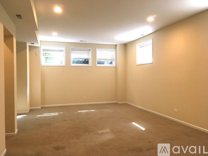 A spacious room with carpeted floor, two windows, and a white wall with a sign that says "AVAIL".