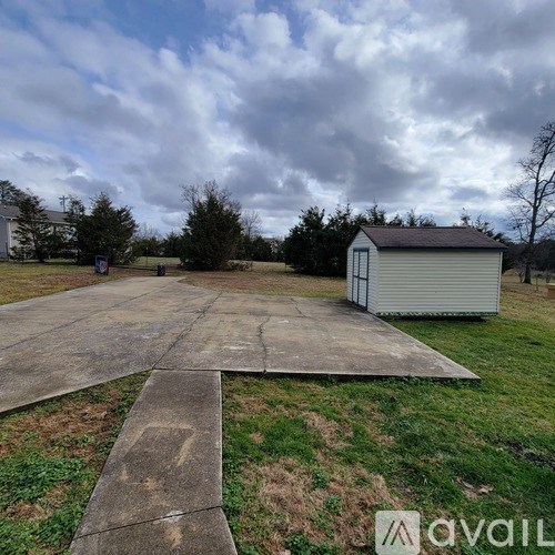 A concrete pathway leads to a small white shed in a grassy field.