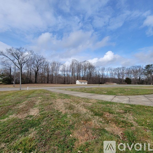 A grassy field with a white building in the distance and bare trees.