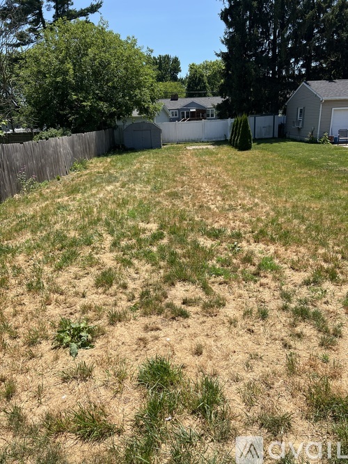 A grassy field with a fence and houses in the background.