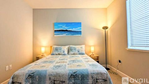 A bedroom with a bed, two lamps, and a painting on the wall.