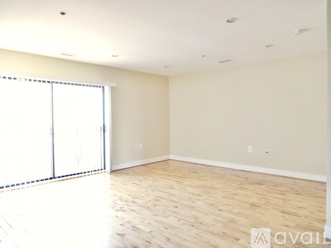 A spacious room with wooden flooring and a sliding glass door.