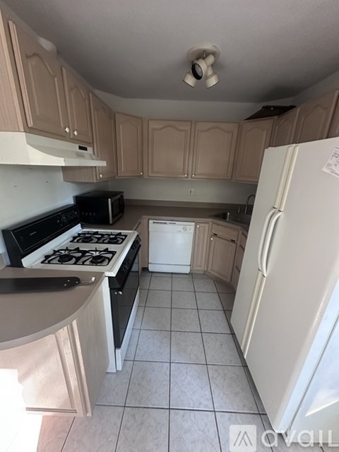 A kitchen with a black stove top oven, white fridge, and wooden cabinets.