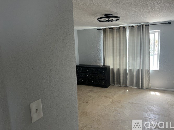 A room with a black dresser and a window with curtains.