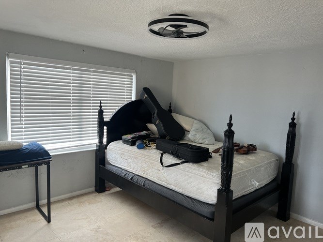 A bedroom with a bed, a table, and a window with blinds.