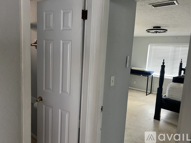 A white door is open to a room with a bed and a desk.