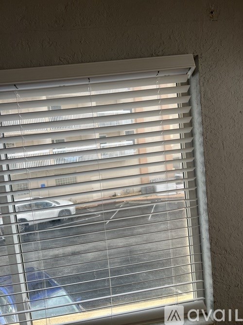 A window with white blinds overlooking a parking lot.